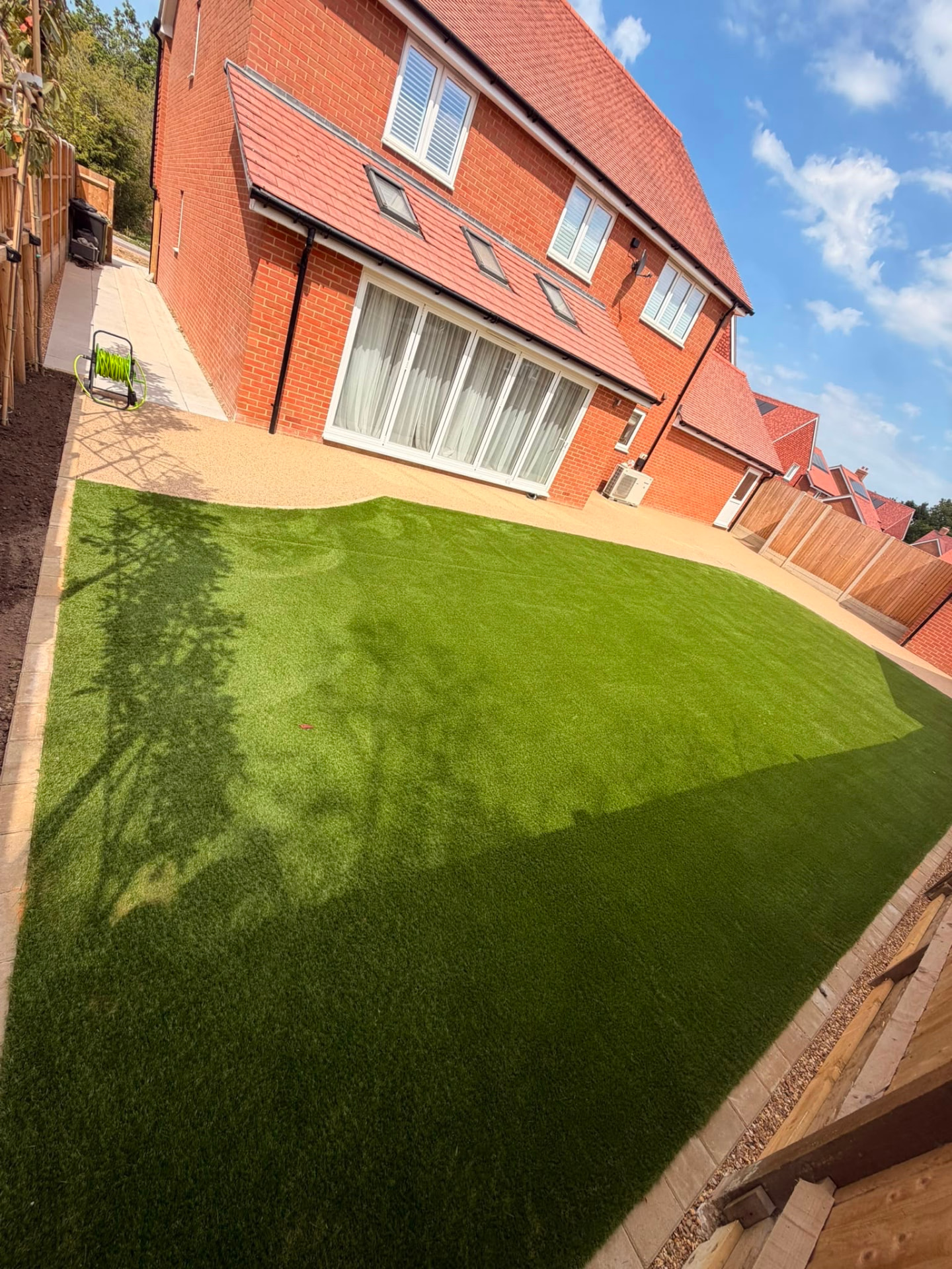Wide artificial lawn with resin bound patio running along bi-fold doors
