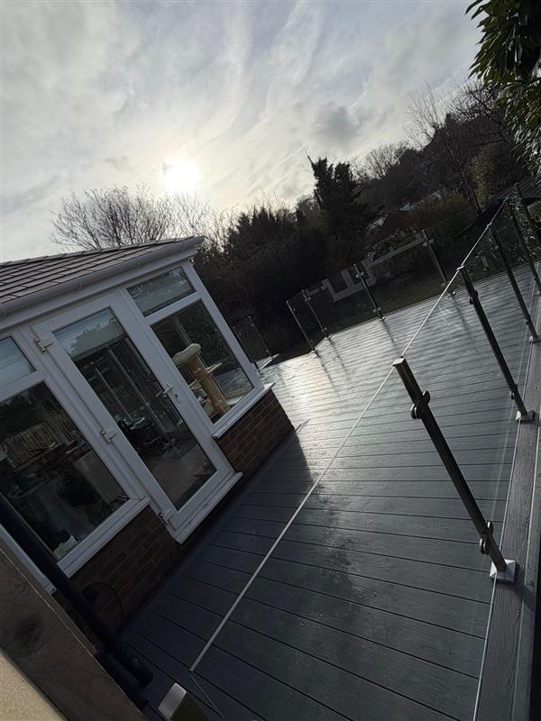 Composite deck with stainless steel and glass balustrade beside a tiled conservatory