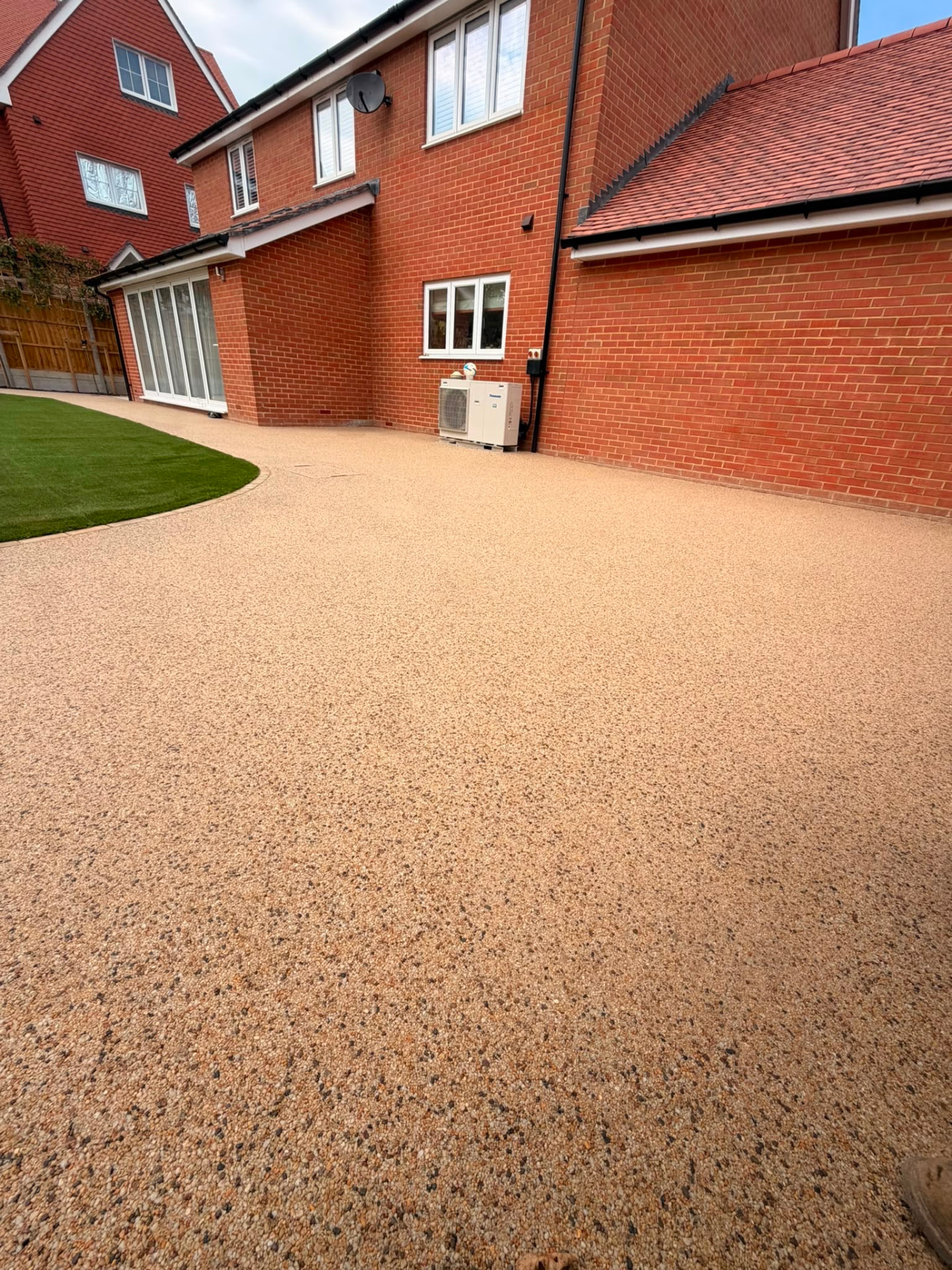 Golden resin bound driveway wrapping around a new build home with curved lawn edge