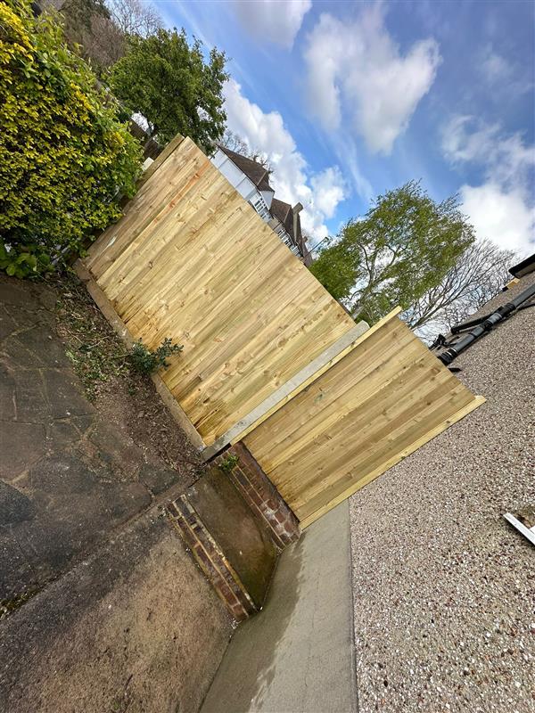 Closeboard fence panels installed on a stepped brick boundary wall beside a driveway