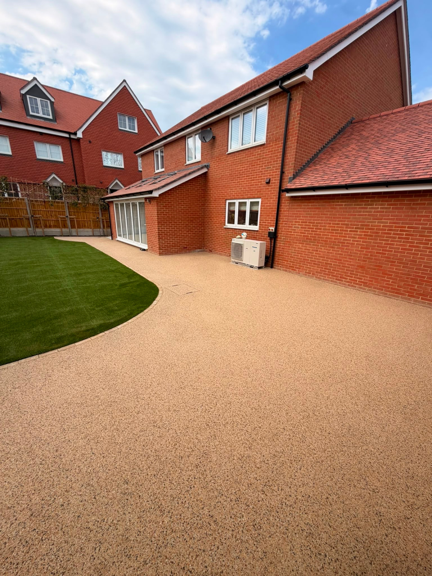 Large resin bound patio and driveway area beside a red brick home with shaped artificial lawn