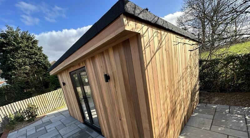 Cedar garden room with felt roof, anthracite doors and paved surround