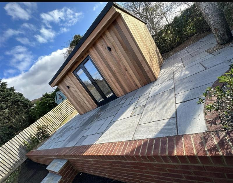 Cedar garden room beside a wide Indian sandstone patio and brick wall