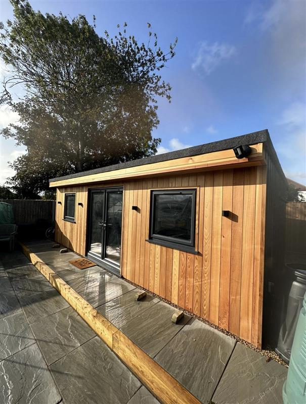 Cedar garden room with double doors and porcelain paving in evening sun