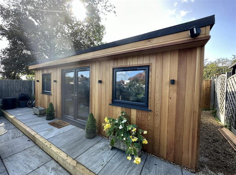 Cedar clad garden office with grey framed windows and sleeper edged paving