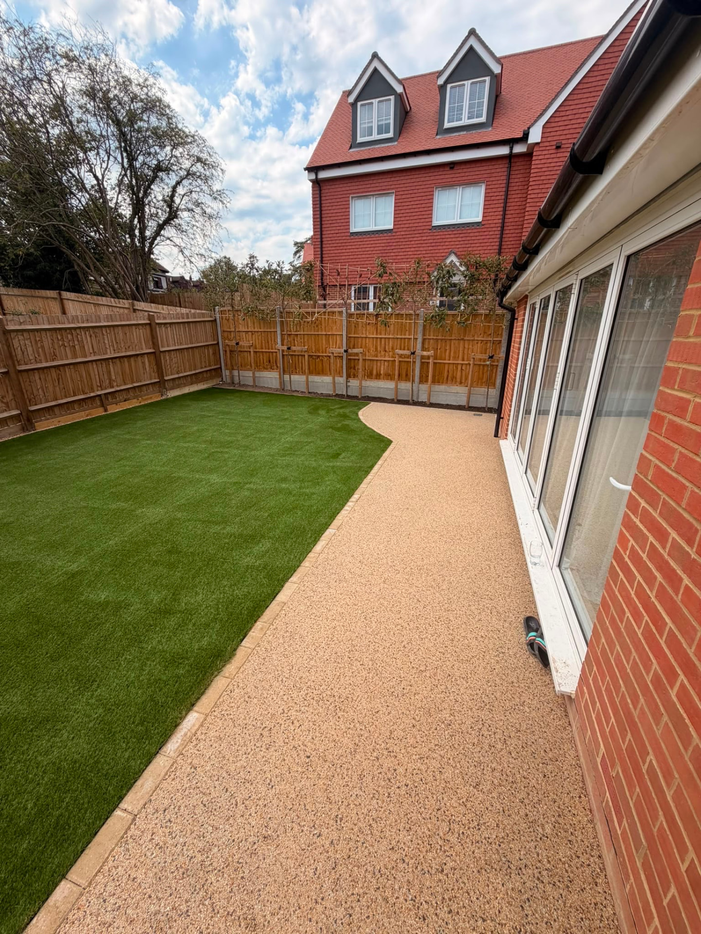 Resin bound pathway with block edging running alongside a fresh artificial lawn and new fencing